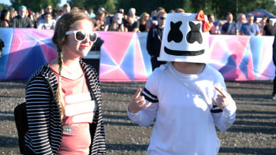 Två besökare på Weekend Festival trivs i solskenet. Den ena har klätt sig helt i vitt, precis som idolen Marshmello.