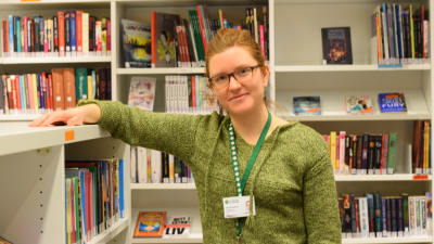 Ungdomsbibliotekarie Lisa Strömsholm framför bokhyllor