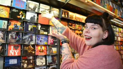 Maria Ahonen i en skivbutik, pekar mot en skiva av Antti Tuisku.