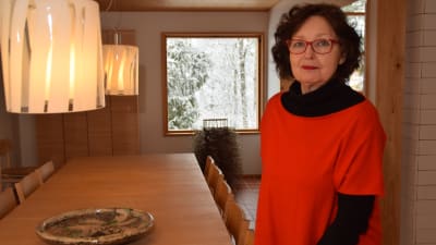 En kvinna klädd i rött och svart och med röda glasögons tår vid ett långt köksbord. Hon heter Karin Widnäs.
