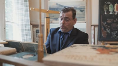 Kantor iklädd mörk kostym sitter bakom tramporgel och sjunger.