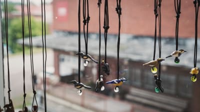 Smycken med fåglar gjorda av glas hänger i ett fönster.
