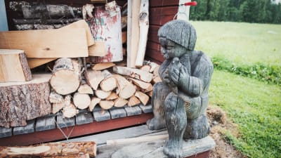Träskulptur föreställande pojke som sitter på en stubbe, intill en vedtrave.