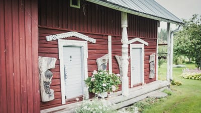 Rödmålat uthus med vita knutar, på väggarna träsnideri föreställande barnansikten i profil.
