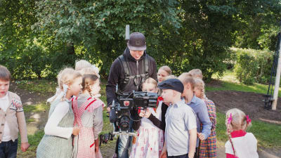 En skock med barn klädda i gammaldags kläder samlas runt fotografen Rasmus Tågs kamera.