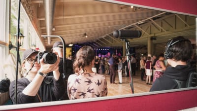 Fotografen Eva Pursiainen tar en bild av sig själv och övriga personer via en spegel inne i en danshall.