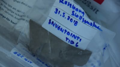 En bild som visar hur arkeologer antecknar sina fynd. På bilden syns en plastpåse där det står Raseborg slottsmalmen 31.5.2018 inventointi. 