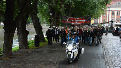 Demonstranter marscherar längs Aura å. En motorcykelpolis åker framför dem.