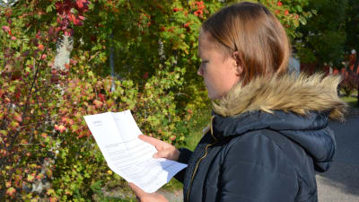 Lotta Björklöf fotograferad från sidan då hon står och tittar på brevet som kom från Caruna.