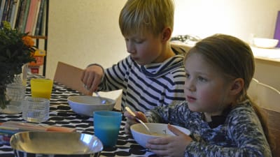 Två barn äter fisksoppa vid matbordet.