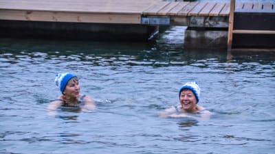 Två glada kvinnor med mössa på huvudet simmar