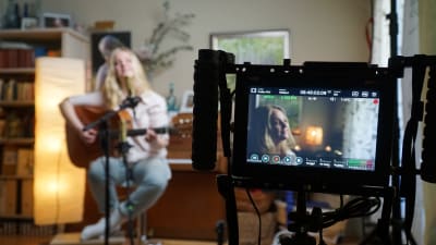 Musikern Tove Ljungqvist spelar gitarr och sjunger framför en videokamera i sitt hem.