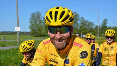 Kristian Kylén, en man med solglasögon, skäggstubb, gul cykelhjälm och gul skjorta, ler mot kameran.
