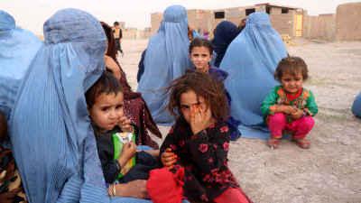 Flyktingar, kvinnor i Burka och deras barn, sitter på sanden i staden Herat.