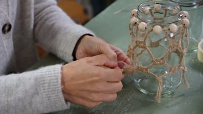 Händer knyter makraméknutar på en glaslykta med makramédekoration