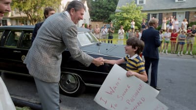 Hymyilevä presidentti Ronald Reagan kättelee pikkupoikaa kadulla Marylandissa. Kuva vuodelta 1983.