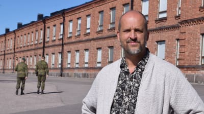 man framför tegelbyggnad och militärer