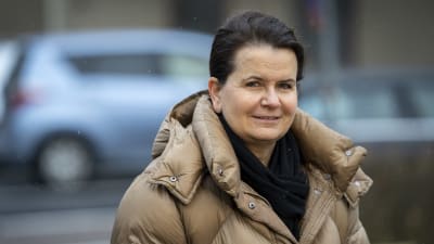 HUS biträdande överläkare Eeva Ruotsalainen står ute i en beige dunjacka. Bakom henne syns bilar parkerade.