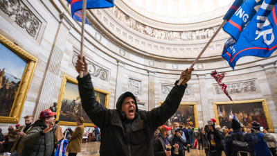 En man viftar med en flagga inne på Capitolium efter stormningen 6.1.2021.