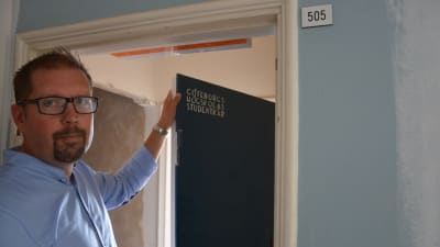 Patrik Fellman håller i en dörr där det står graverat "GÖTEBORGS HÖGSKOLAS STUDENTKÅR"