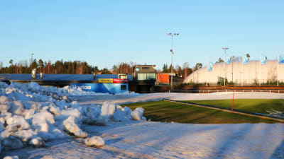 En snöhög till vänster framför grönt gräs och en kupolformad bollhall.
