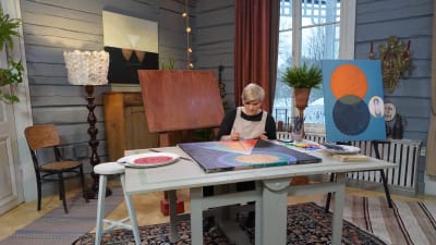 Camilla Forsén-Ström sitter vid ett bord målar en tavla enligt modell från Hilma af Klint 