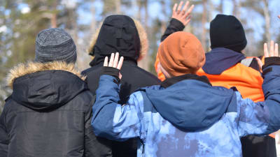 Fyra barn med ryggarna mot kameran viftar med händerna. De är vinterklädda.