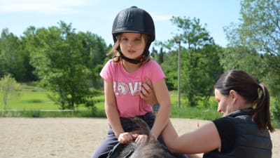 Sexåriga Ellen Lankinen uppe i sadeln medan mamma Paula hjälper till.