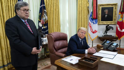 William Barr står vid ett skrivbord. Vid skrivbordet sitter Donald Trump.