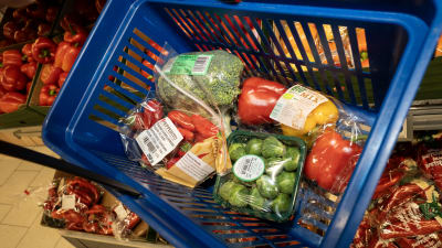 Inplastade grönsaker i en varukorg i plast från en matbutik.