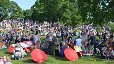 Människor i färggranna kläder håller picknick i en park efter en prideparad.