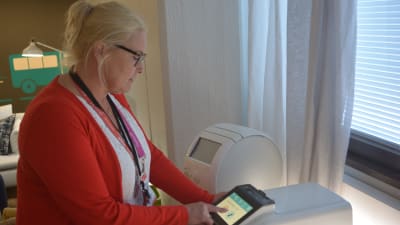 Viveka Bergdahl-Silvennoinen, som jobbar som teamförman på Helsingfors stads servicecentral, visar upp hur en läkemedelsrobot fungerar