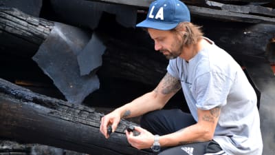 Man undersöker träbitar efter husbrand.
