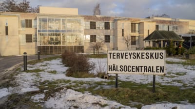 En skylt framför en byggnad. På skylten står det hälsocentralen på finska och svenska.