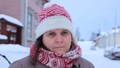 En kvinna med rödvit mössa och halsduk står på en snöklädd gata.