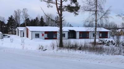 En radhus byggnad med vita och röda väggar. Framför byggnaden finns två träd.