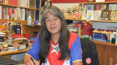 Leung Kwok-hung med långt hår sitter vid sitt skrivbord. 