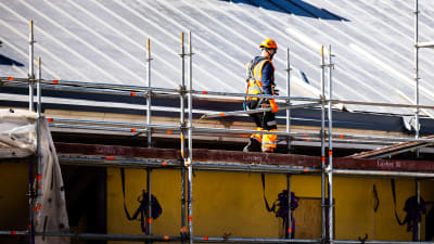 En byggnadsarbetare går på en ställning vid ett tak.