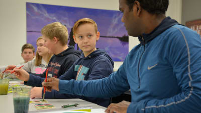 Elever och Venkat sitter vid ett bord och målar. Den ena pojken tittar på Venkat. 