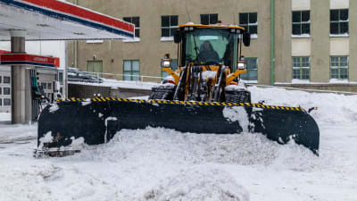Traktor röjer snö på gård.