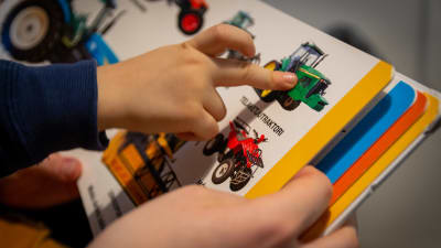 Ett barn pekar med fingret på en traktor i en bok. 
