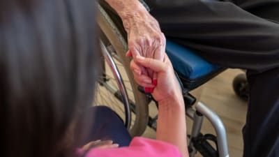 Skötare håller in en äldre människas hand.