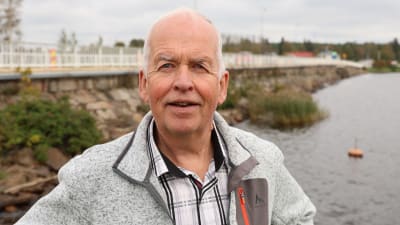 En man med kort grått hår. I bakgrunden syns en gammal stenbro.