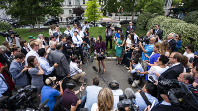 Sarah Sanders omringad av journalister, mikrofonstänger och kameror på Vita husets gård.