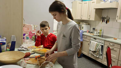 En cirka tioårig flicka står och lagar smörgåsar. En yngre pojke tittar på.
