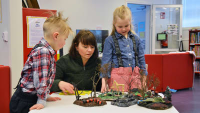 Åsa Rosenberg tittar på en utställning på Nagu bibliotek tillsammans med barnbarnen Jasper och Nova. 