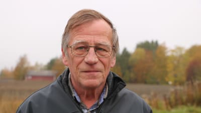 En man med kort, lite gråaktigt hår och glasögon står framför en åker.