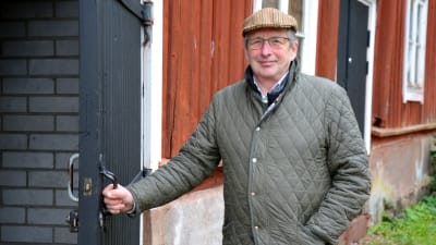 Äldre man öppnar en dörr till en gårdsbyggnad.