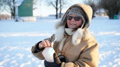 kvinna i vinterkläder som håller på att ta fram ett istegel ur ett mjölkpaket