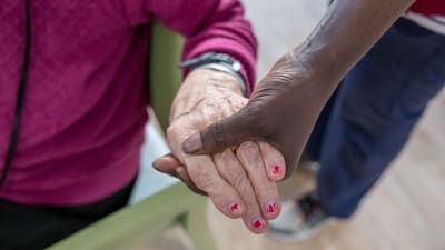 En skötare håller en pensionär om handen.